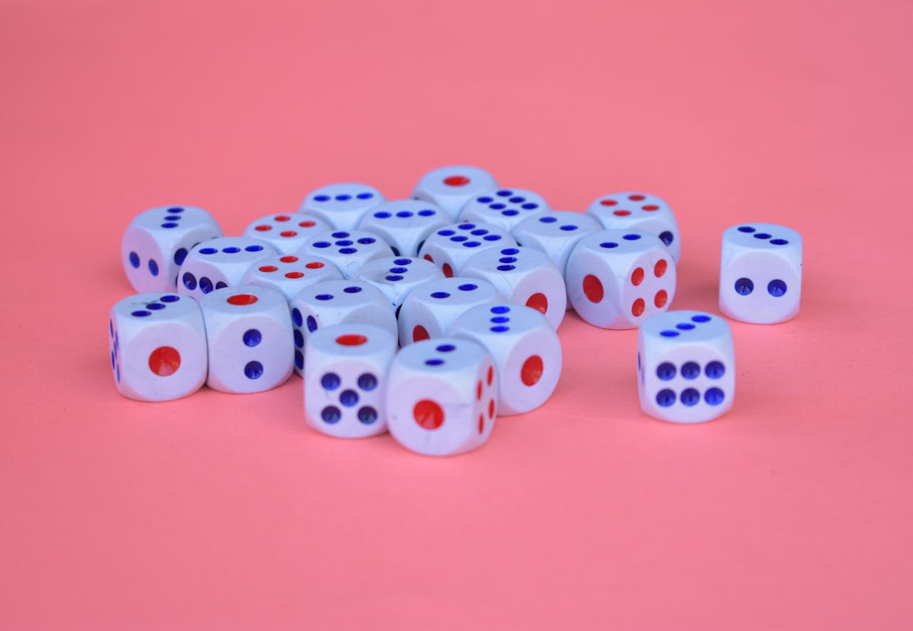 A collection of white dice with red and blue dots arranged on a pink surface.