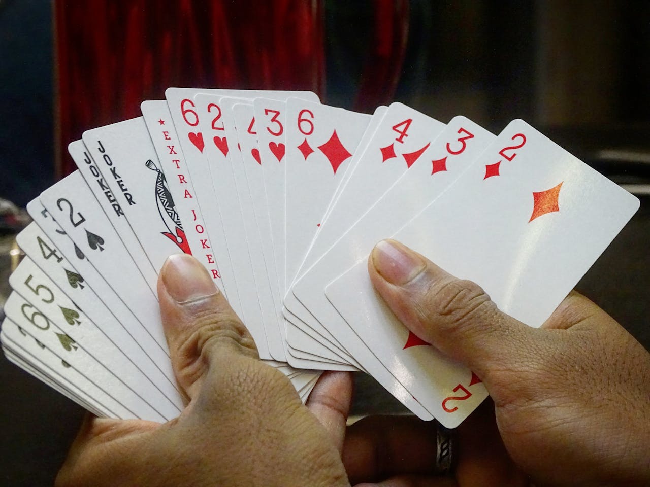 Focused view of hands holding playing cards, emphasizing a mix of clubs, hearts, and jokers.
